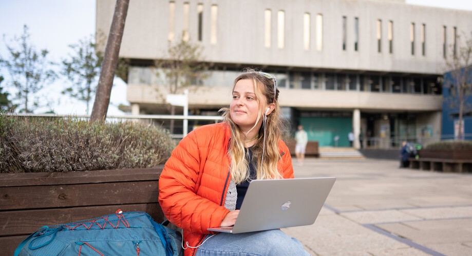 Myfyriwr yn gweithio ar eu gliniadur o flaen Llyfrgell Hugh Owen | Student working on their laptop outside the Hugh Owen Library. 